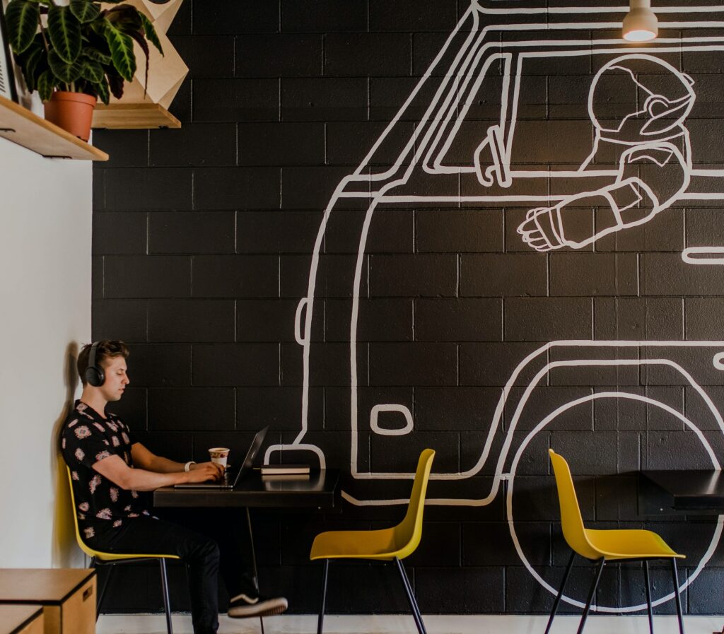 A man sitting in a coffee shop working on his laptop using social listening content tools