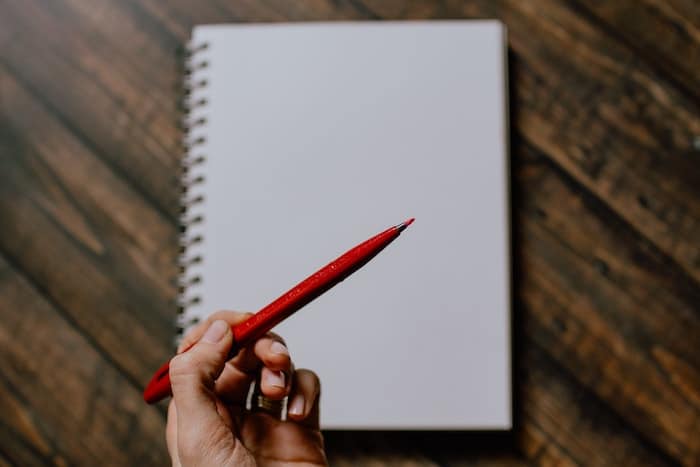 Hand holding red pen over blank notebook page