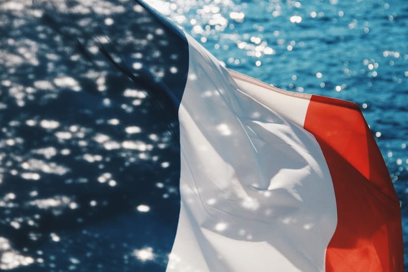 Photo of French flag waving in the wind, with the ocean in the background