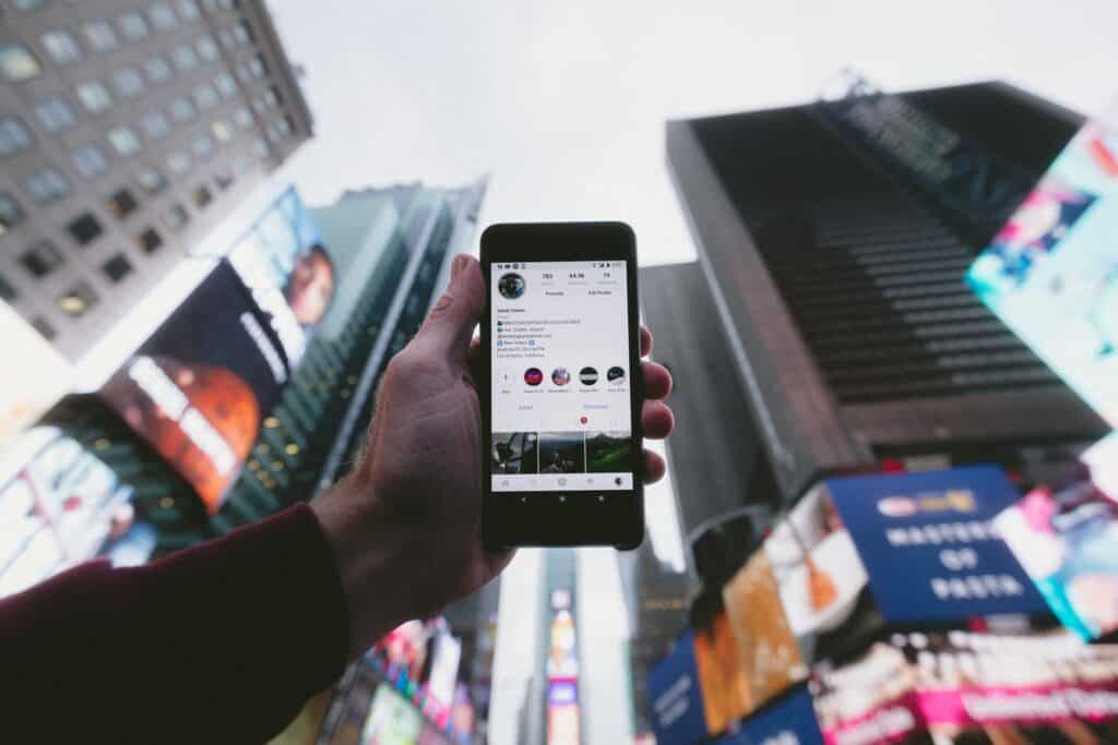 A person holding up a phone in the city with a local Instagram account on the screen