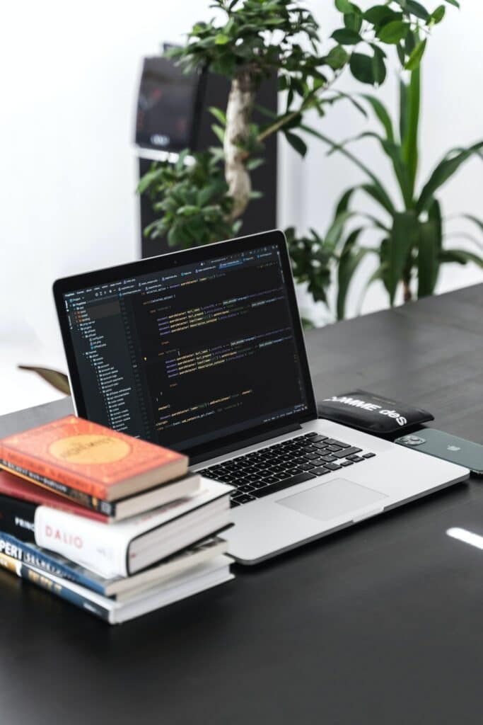 A pile of books next to a laptop showing website code with hreflang tags