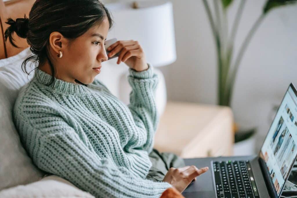 A young woman in bed online shopping on a website with multilingual capabilities