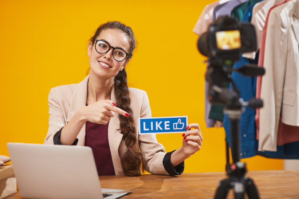 Portrait of young woman holding LIKE word and smiling at camera while filming video for global social media accounts