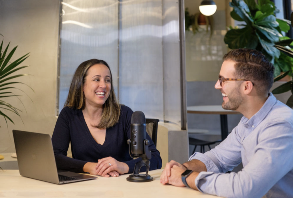 Two people from the VeraContent team smiling each other while recording a podcast in a coworking spot