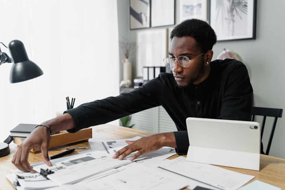 Man sitting at a desk with piles of paper and an ipad