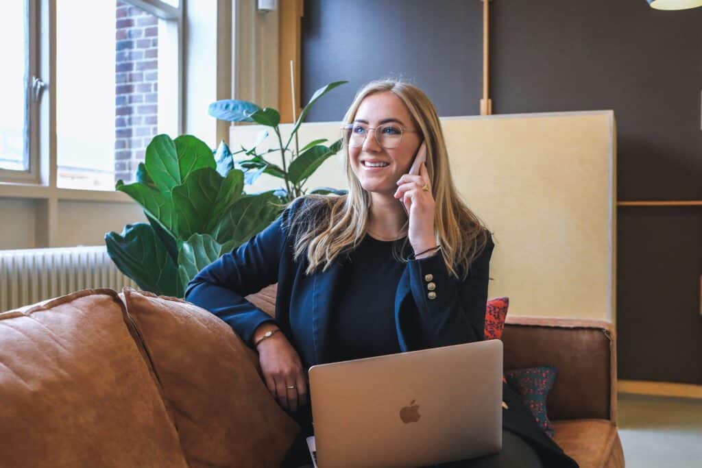 Global marketing manager sitting on sofa on the phone with laptop on her lap