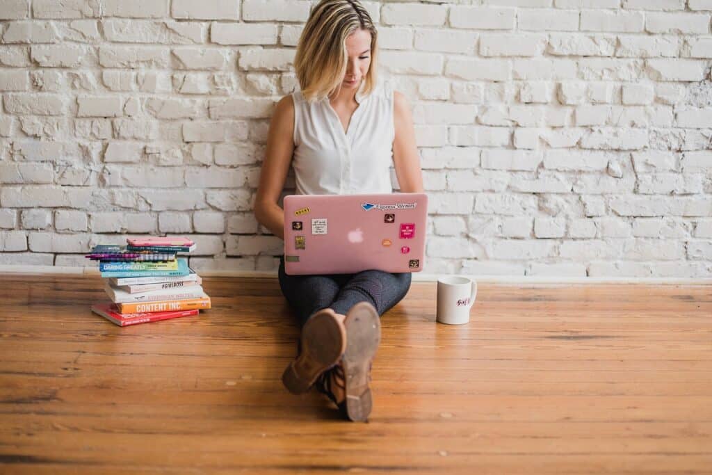 Woman sitting on the floor with a laptop and pile of books next to her