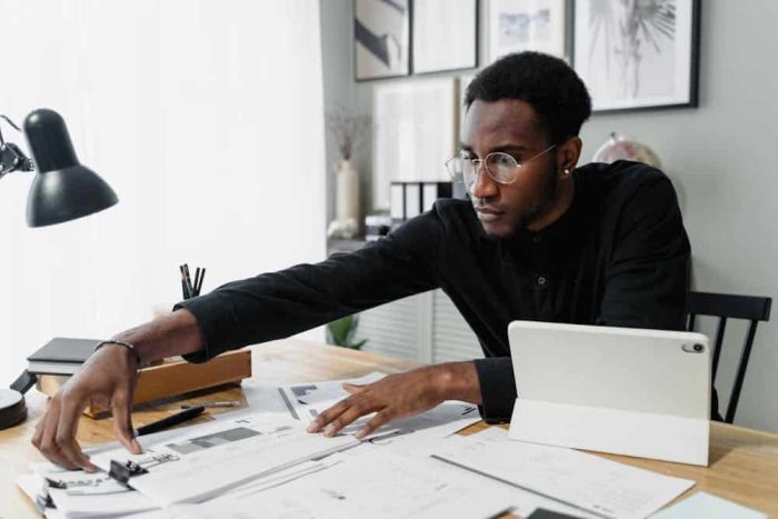 Man sitting at a desk with piles of paper and an ipad